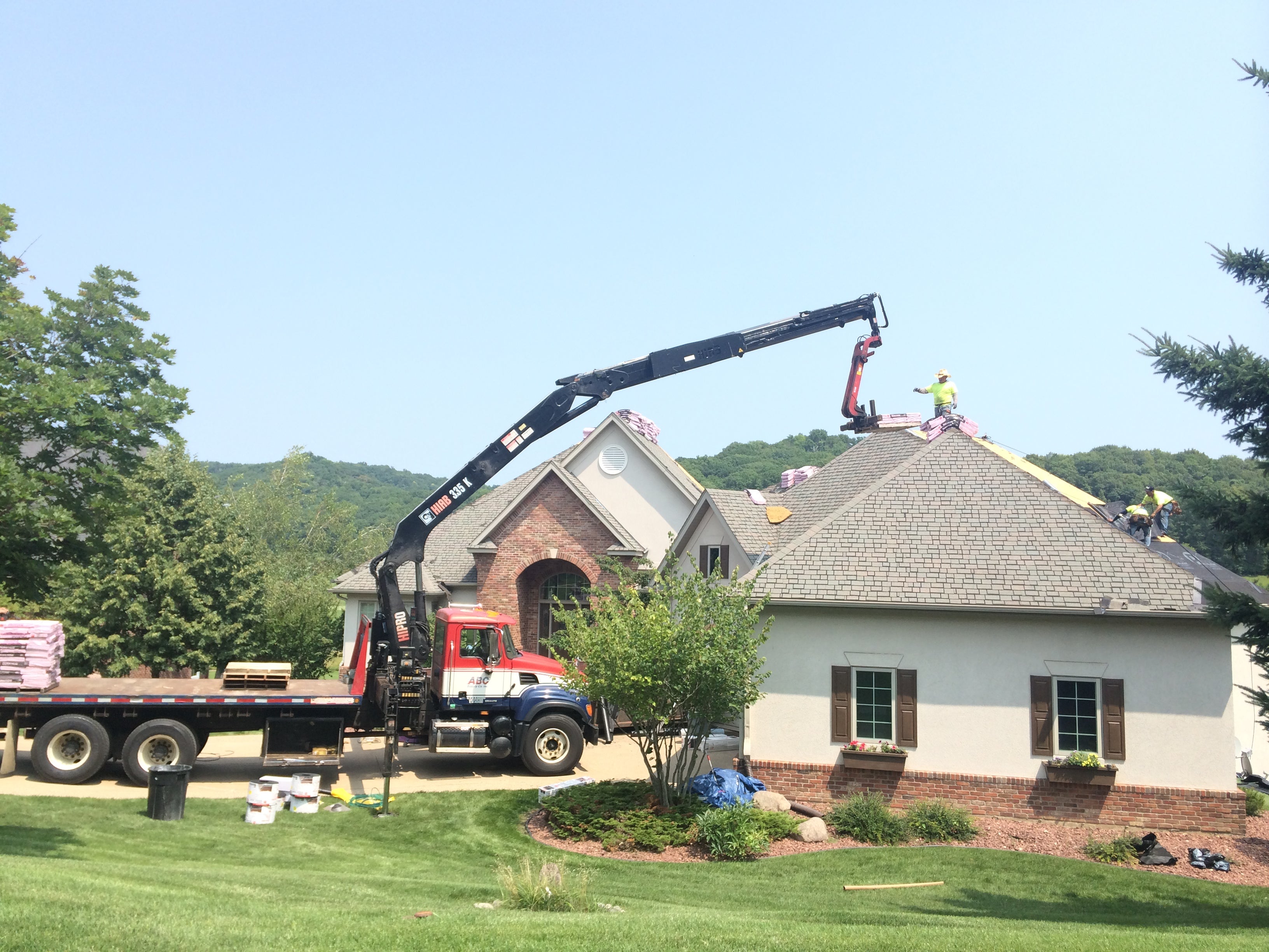 Roofing work being done on a house with a crane and truck in the foreground.